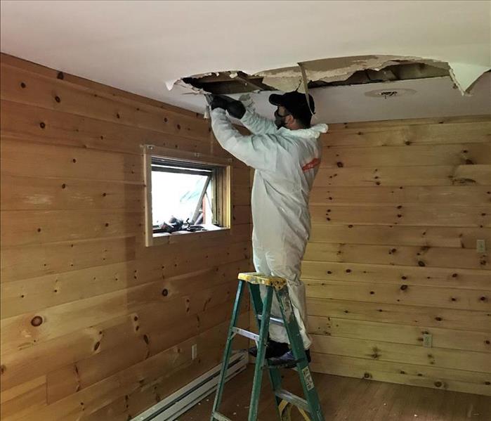 A ceiling with water damage and a SERVPRO technician standing on a ladder