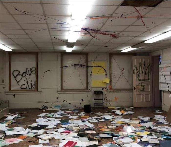 Inside of a commercial space vandalized by spray paint with books and papers scattered throughout the room.