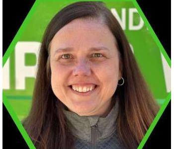 Woman in gray jacket with brown hair and green truck in background.