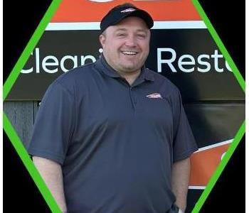 Male SERVPRO employee in black shirt leaning on green truck in front of red building.