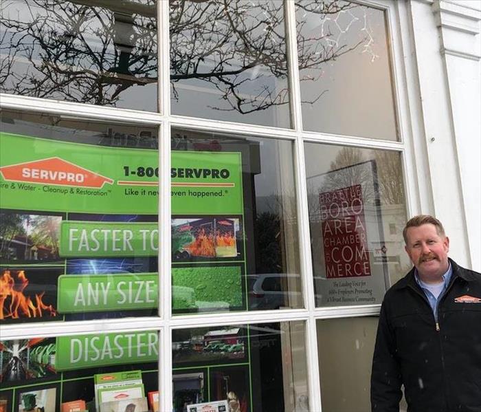 SERVPRO Owner standing in front of a large window display on a street which features a colorful backdrop of his business.