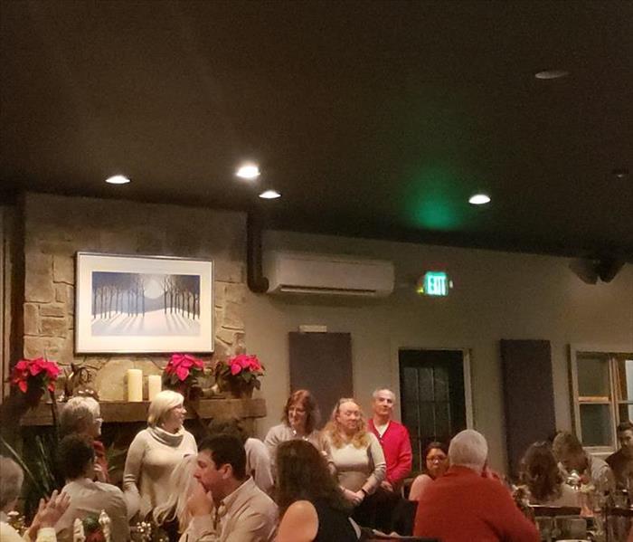 photo of people inside a restaurant, some of them at the front of the room standing and speaking to the group