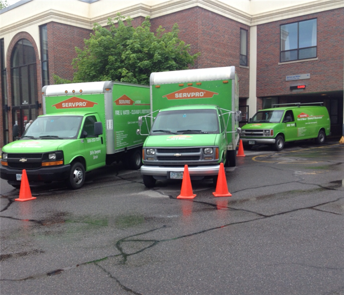 Two green SERVPRO trucks parked in front of a 2-story brick commercial building.