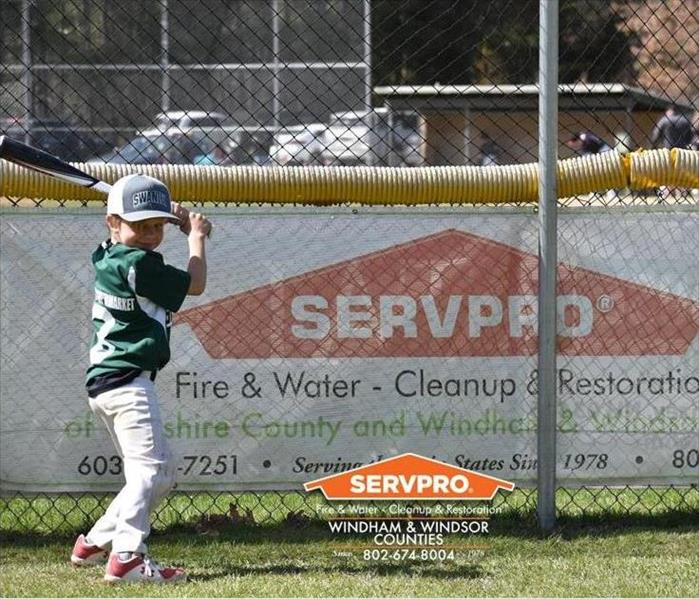 Youth baseball player with a bat standing in front of SERVPRO banner.