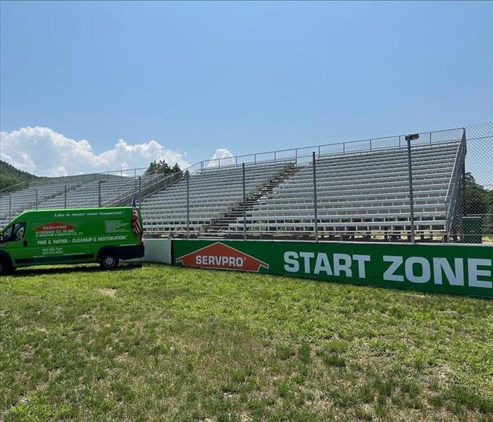 Green SERVPRO van parked next to wall of race track with large green banner that reads "SERVPRO START ZONE"