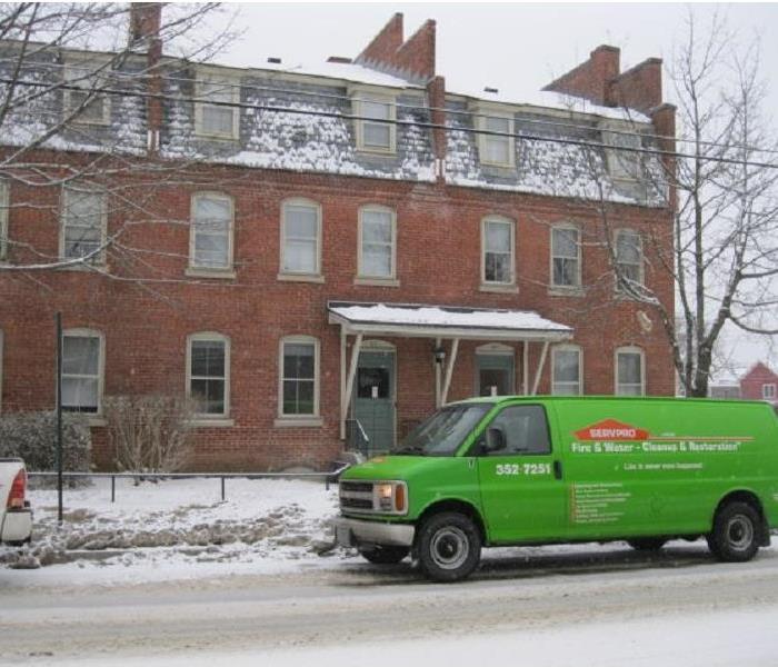 SERVPRO truck parked in front of a large brick apartment building with snow on the ground.
