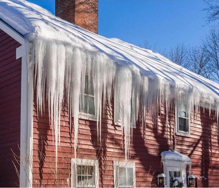 Snow and ice buildup on the edge of a roof on a red house causing large icicles to form.