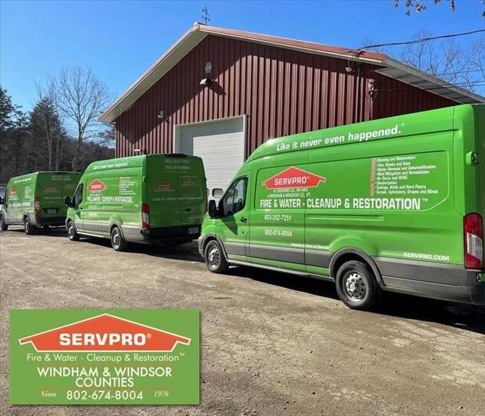 Three green SERVPRO vans parked in front of large red metal building.